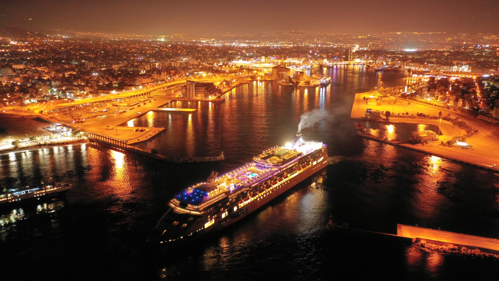 Aerial drone night shot of beautiful illuminated port of Piraeus and huge cruise liner departing to Aegean popular destinations, Attica, Greece