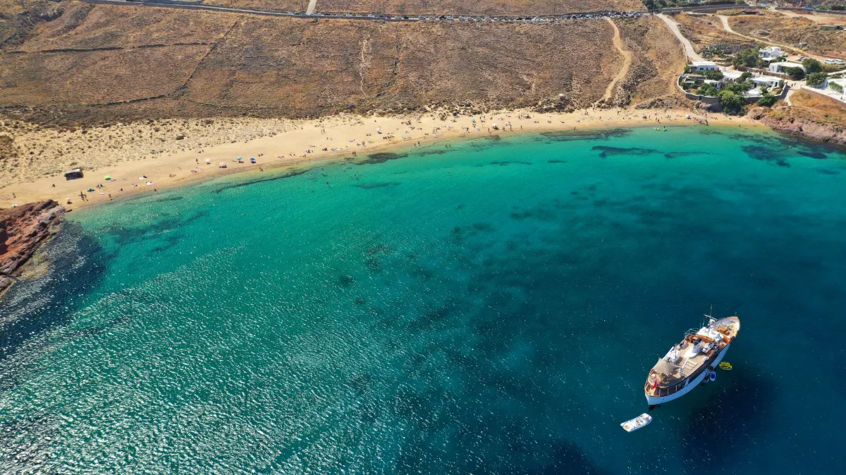 Aerial view of a yacht anchored off a sandy Mykonos beach with sunbathers