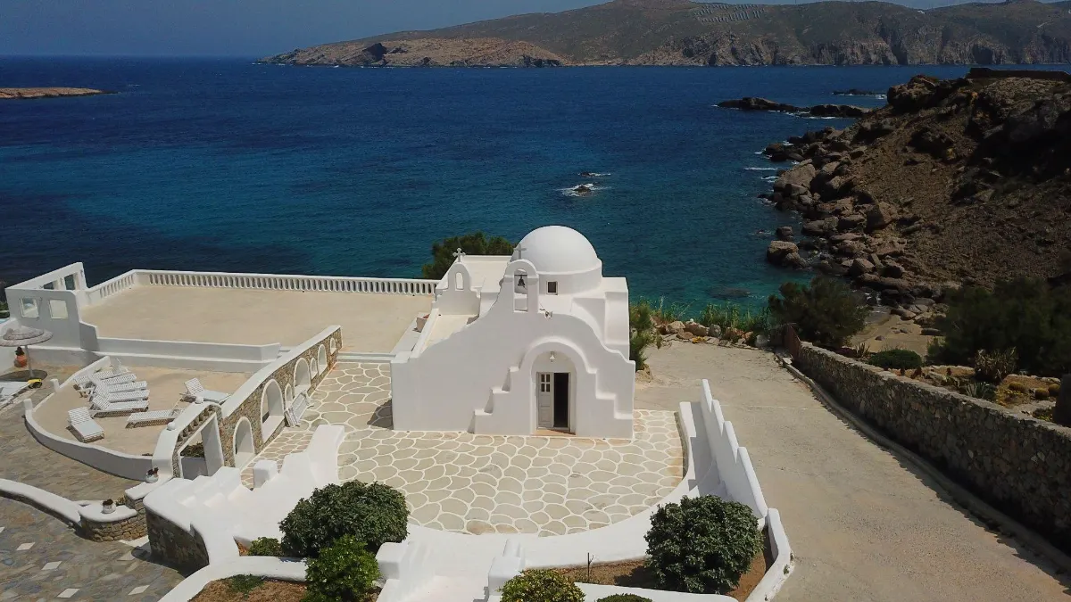 Whitewashed chapel with a domed roof overlooking a deep blue Aegean bay
