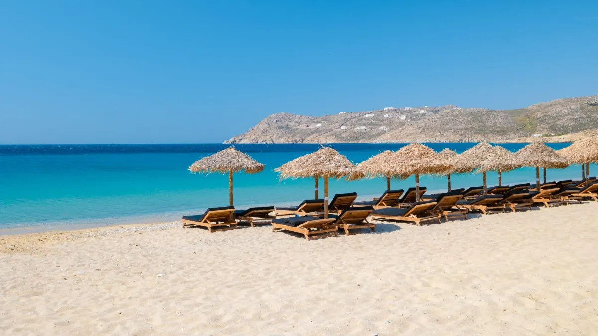 Straw umbrellas and sun loungers on a sandy Mykonos beach by turquoise water Elia Beach Mykonos 1