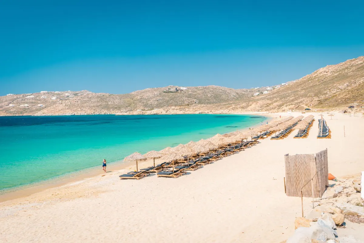 Rows of straw beach umbrellas along a curved sandy shore in Mykonos
