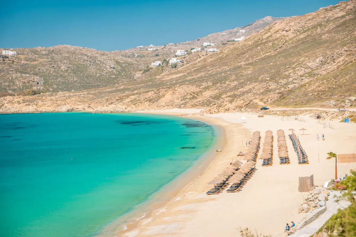 Wide view of a sandy Mykonos bay with sun loungers and turquoise water