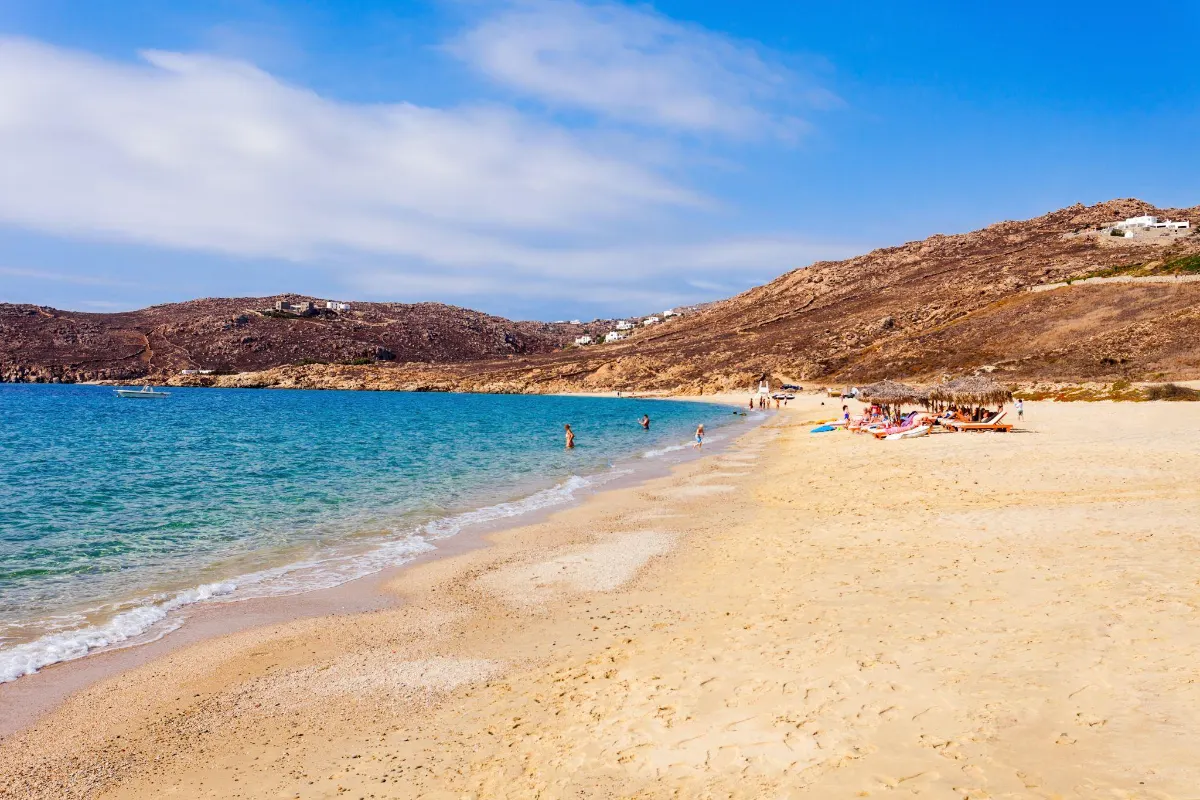 Golden sandy beach in Mykonos with swimmers and hills in the background