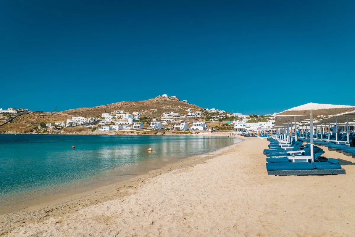 Empty stretch of sand with beach loungers facing a calm Mykonos bay