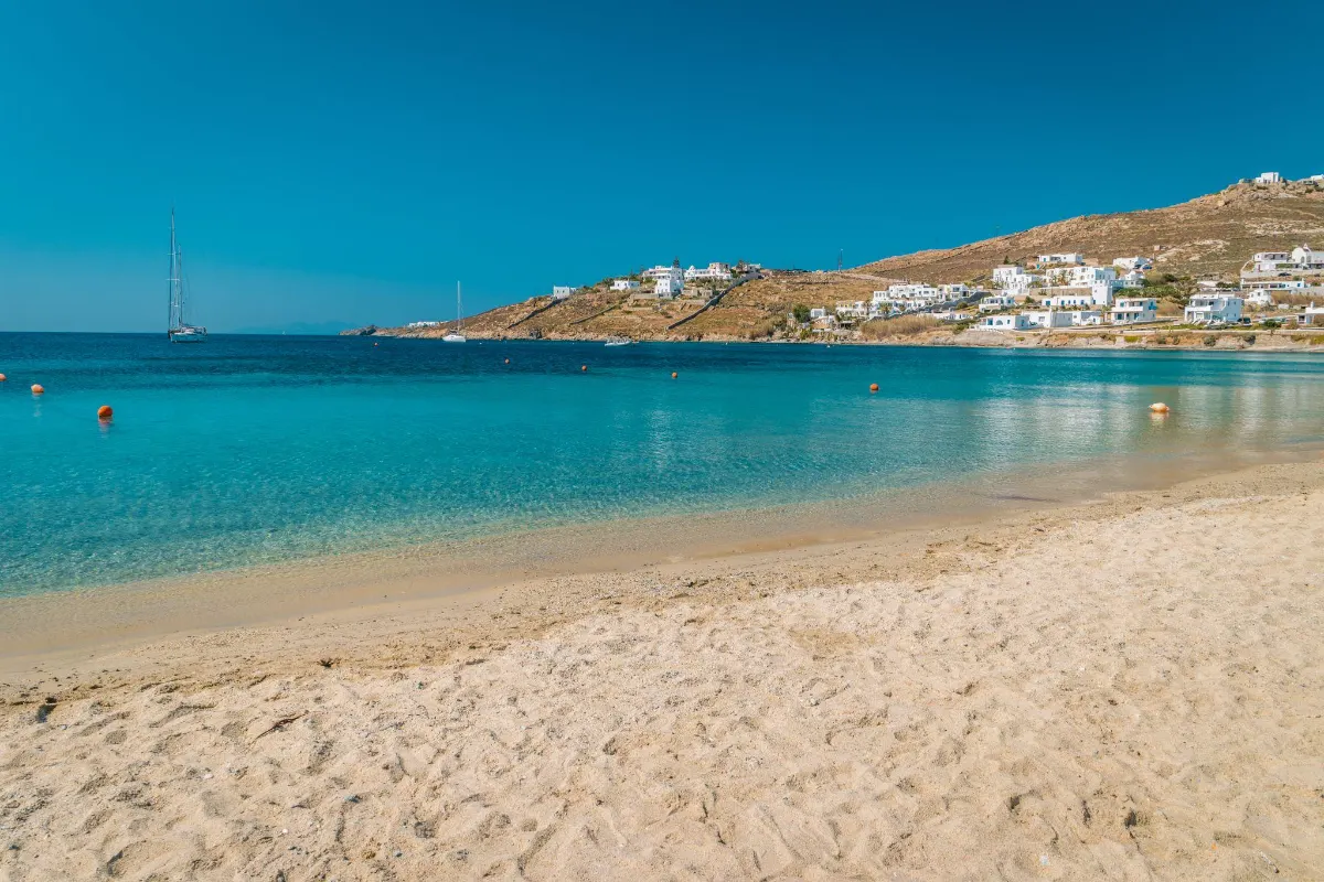 Sailboats anchored in a turquoise Mykonos bay with a whitewashed village