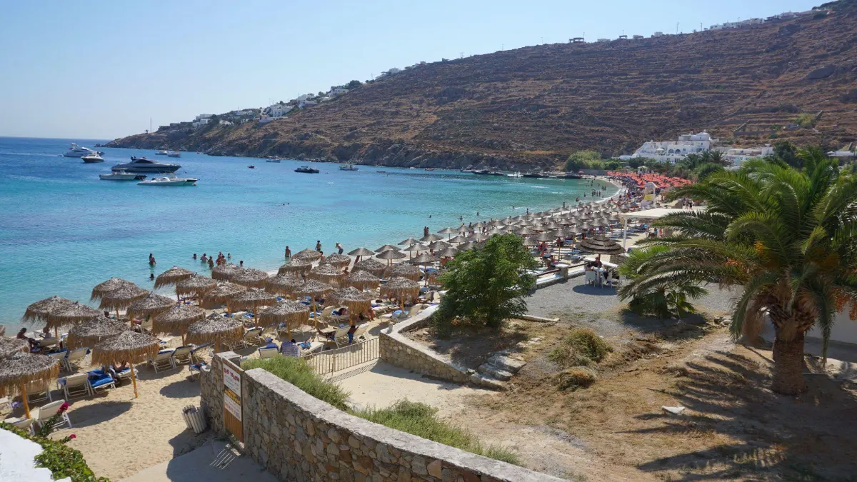 View over a Mykonos bay lined with straw umbrellas and anchored yachts