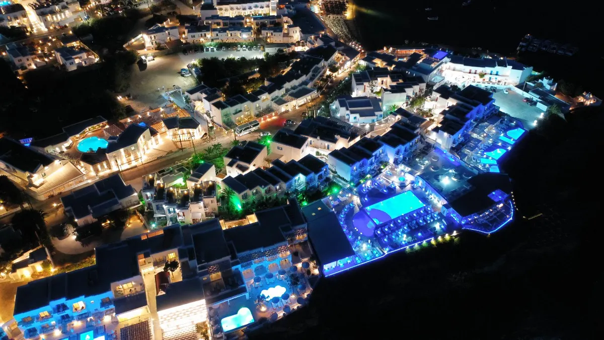 Nighttime aerial view of an illuminated Mykonos resort with glowing pools